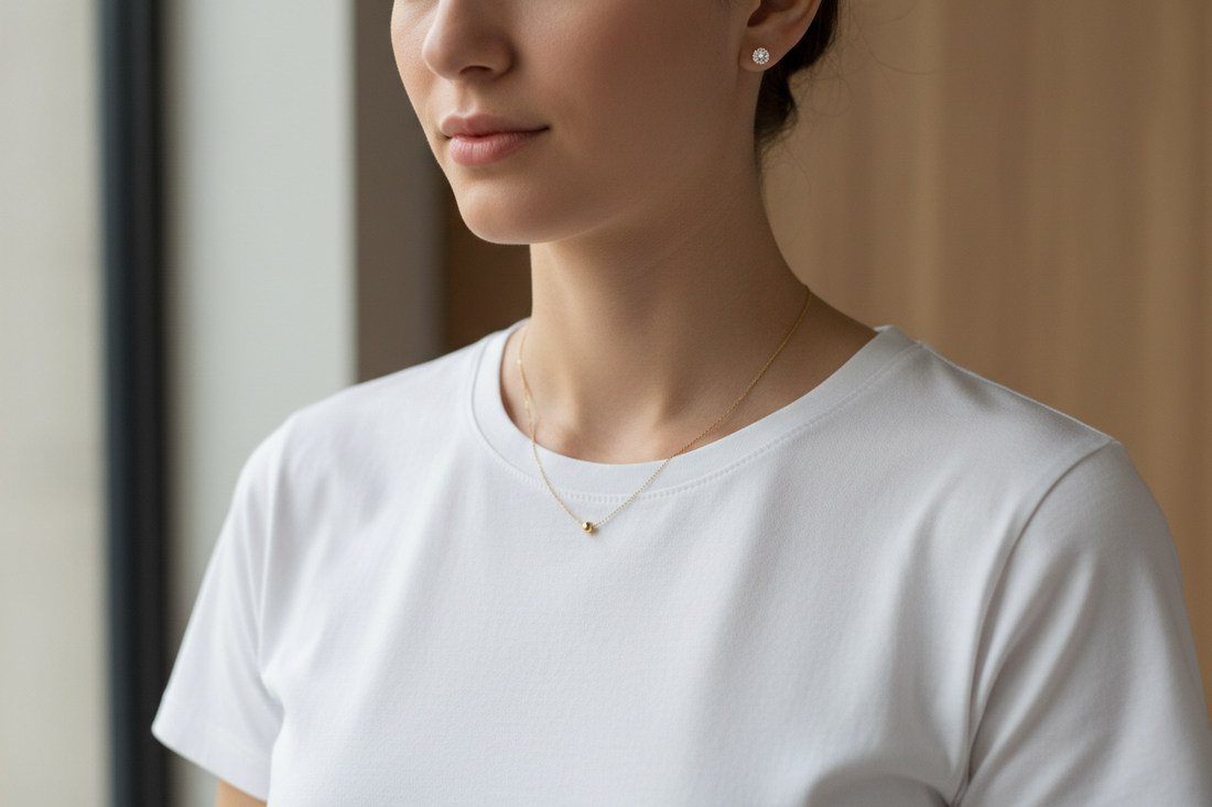 Detalle del cuello de una mujer con una camisa blanca básica luciendo una cadena de oro muy fina y unos pequeños pendientes